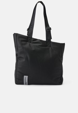 Μαύρη νάιλον τσάντα tote με ορθογώνιο σχήμα, υφή και μακριές λαβές που φέρουν το λογότυπο της μάρκας. Περιλαμβάνει μια μικρή ασημένια ετικέτα.