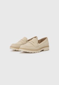Mocassins beiges en daim avec une texture lisse, présentant un accent cousu sur le devant et une semelle en caoutchouc contrastante.