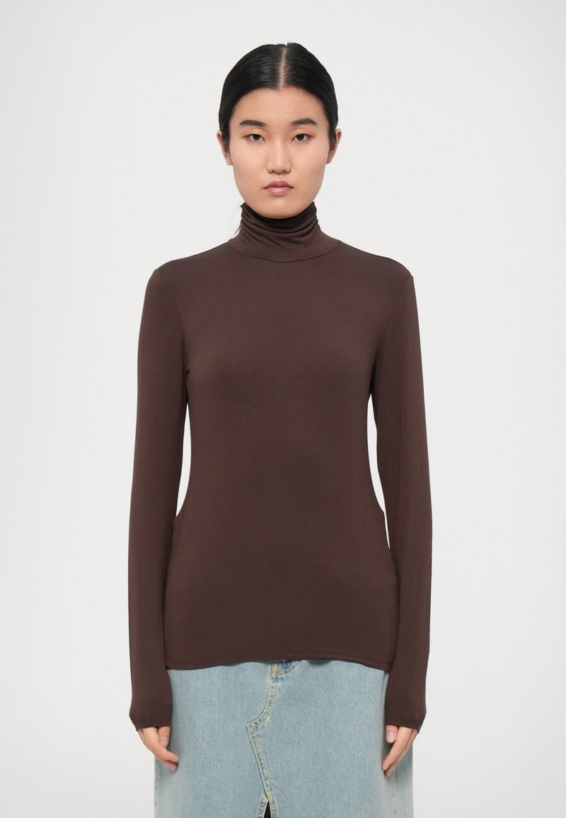 Brown turtleneck sweater in soft fabric, featuring long sleeves and a fitted silhouette, paired with a light denim skirt.