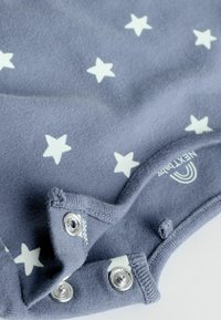 Bodysuit pour bébé gris avec motif d'étoiles blanches, doté de boutons-pression en métal à l'arrière et d'une texture en coton doux.