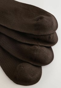 Quatre paires de chaussettes montantes marron foncé soigneusement empilées, avec des coutures visibles aux orteils, sur un fond blanc.