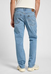 Jeans de mezclilla azul claro con un corte recto. Presentan dos bolsillos traseros y un parche de cuero marrón de la marca en la cintura.