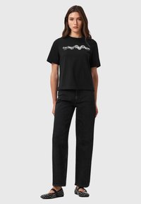 T-shirt nera in cotone con maniche corte e vestibilità rilassata, che presenta testo grafico bianco. Abbinato a jeans neri a vita alta e ballerine con borchie.