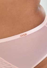 Ljust rosa mesh-lingerie med en mjuk midjeresår och platta sömmar, med subtil brandingdetalj på övre kanten.