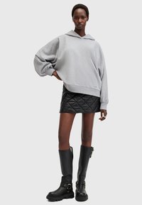 Felpa grigia oversize con cappuccio, abbinata a una mini gonna nera trapuntata e stivali neri alti fino al ginocchio con dettagli in metallo.