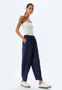 Marineblaue, locker sitzende Hose mit elastischem Bund und Seitentaschen, kombiniert mit einem weißen Tanktop. Modell trägt weiße Sneakers.