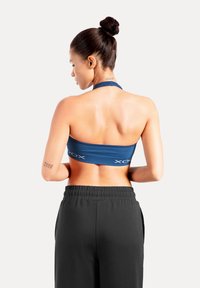 Sportbeha in marineblauw met geribbelde textuur en verhoogd logodetail, gecombineerd met losse zwarte joggingbroek met elastische tailleband.