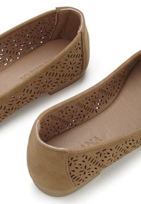 Beige Ballerinas aus strukturiertem Material weisen an den Seiten laserperforierte Muster auf, haben ein glattes Innenfutter und einen niedrigen, stabilen Absatz.