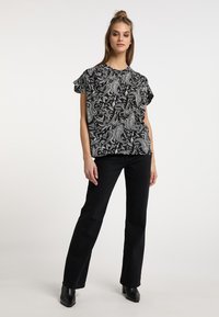 Sort og hvid paisley mønstret bluse med korte flæseærmer, parret med sorte straight-leg jeans og sorte hælstokke.