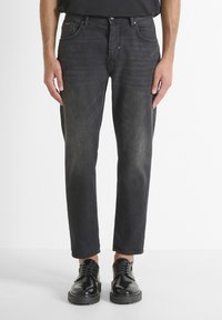 Jeans de mezclilla negra con corte recto, cinco bolsillos, un leve desvanecimiento y un ajuste relajado. Combinados con zapatos negros de cordones.