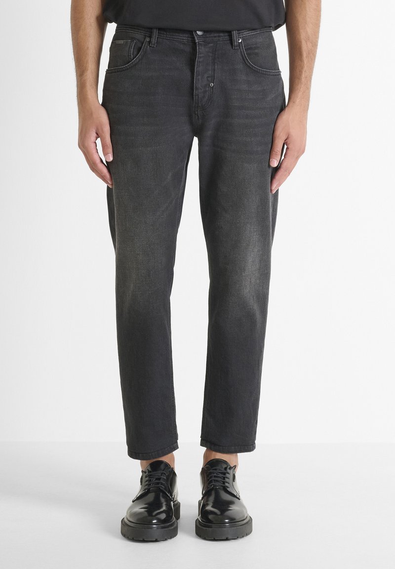 Jeans de mezclilla negra con corte recto, cinco bolsillos, un leve desvanecimiento y un ajuste relajado. Combinados con zapatos negros de cordones.