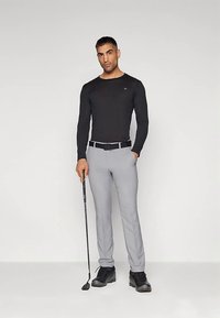 Hosszú ujjú fekete ing kerek nyakkivágással, világosszürke nadrággal párosítva. A modell golfütőt tart, fekete cipőt visel.