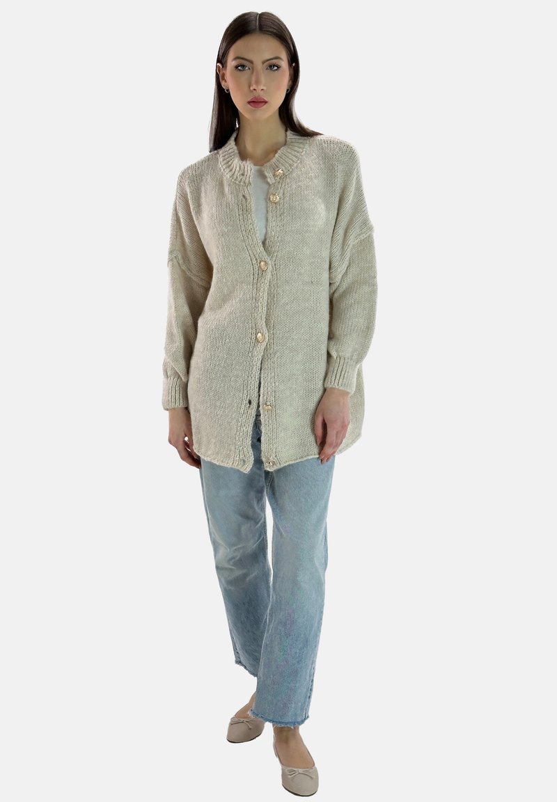 Krämfärgad stickad cardigan med en strukturerad yta, med V-ringning, långa ärmar och dekorativa knappar. Bärs över ljusblå jeans.