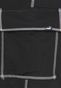 Bolsa de tela negra con detalles de costura blanca y una pequeña etiqueta con el logo de Puma. La textura parece suave y ligeramente elástica.