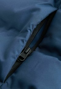 Gros plan sur une fermeture éclair noire partiellement ouverte sur un tissu matelassé bleu, montrant la texture et les plis du tissu.