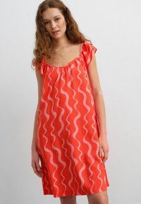 Rode mouwloze jurk met roze golfpatronen, geplooide halslijn en ruffles op de schouders. Gemaakt van lichtgewicht stof.