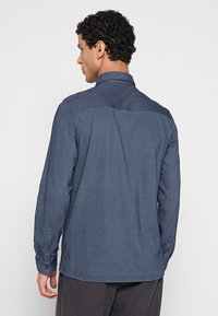 Marineblauw shirt met lange mouwen, gemaakt van gestructureerde stof, voorzien van een puntkraag, zijnaden en manchetten met knopen.