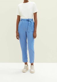 Jasnoniebieskie spodnie związywane w talii, wykonane z miękkiego materiału. W połączeniu z gładką białą koszulą z krótkim rękawem i beżowymi trampkami.