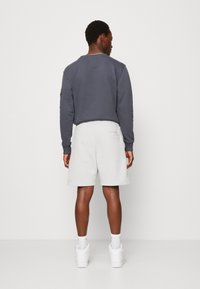 Szary bawełniany sweatshirt z prążkowanymi mankietami, w połączeniu z jasnoszarymi szortami na elastycznej talii. Całość uzupełniają białe sneakersy. Widok z tyłu.