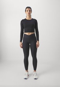 Zwarte cropped top met lange mouwen, gecombineerd met hoge zwarte leggings. Gelaagde stof en strak ontwerp, compleet met witte sportschoenen.