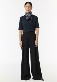Czarna, prążkowana bluzka z krótkimi rękawami, połączona z czarnymi, szerokimi spodniami o wysokim stanie oraz drukowanym szalikiem związanym wokół szyi.