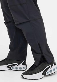 Pantaloni sportivi neri con cerniere laterali, abbinati a sneaker bianco e nere con suola a bolla, parte superiore testurizzata e dettagli in mesh.