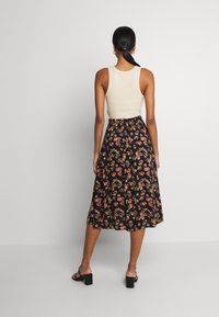 Jupe midi noire à motifs floraux avec une taille froncée, associée à un débardeur beige. Dispose d'une coupe décontractée et de motifs floraux subtils.