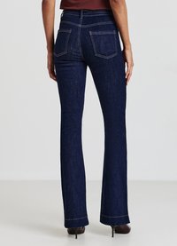 Jean flare bleu foncé avec une taille haute, présentant un design épuré, des jambes droites et des coutures contrastantes. Équipé de deux poches arrière.
