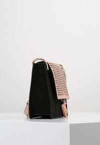 Borsa a mano in pelle nera con patta rosa traforata, ferrature dorate e forma strutturata. Include un pendente decorativo attaccato a una tracolla.