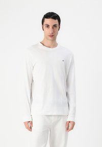 Weißes Langarm-T-Shirt aus weichem Stoff, mit Rundhalsausschnitt und dezentem Logodetail. Lässiges Design mit bequemer Passform.