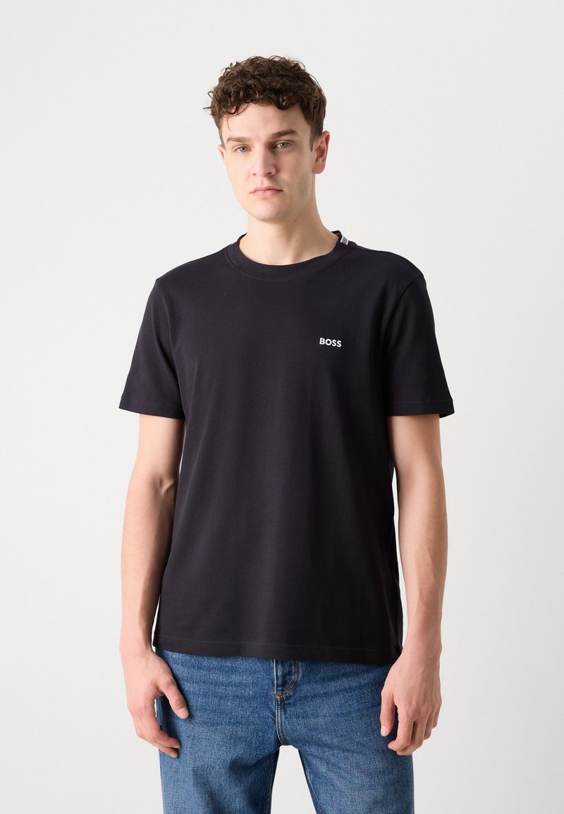 T-shirt en coton noir à manches courtes, col rond, avec un petit logo blanc "BOSS" sur la poitrine gauche. Associé à un jean en denim bleu.