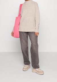 Ljusbeige tröja, grå jeans och kraftiga beige sneakers. Rosa tote-väska på axeln. Mjuk textur, avslappnad passform och synlig sömnad.