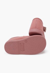 Zapatillas de tela rosas con un acabado texturizado, punta redondeada y tira al tobillo. Suela de goma con una marca minimalista y bordes suaves.