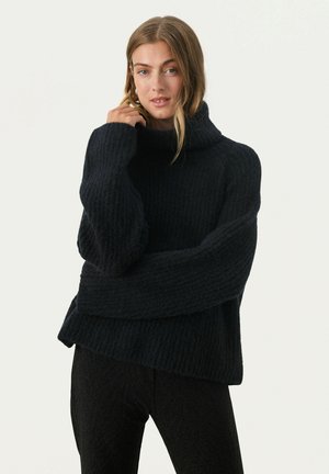Dikke zwarte gebreide trui met een hoge kraag, voorzien van oversized mouwen en een gestructureerd patroon. Draag het over donkere, gestructureerde broeken.