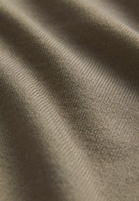 Tejido texturizado en un beige apagado, con un patrón acanalado y sutiles variaciones en el tono, creando una apariencia suave y tejida.