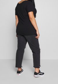 Svart kortärmad topp med spetsurringning, kombinerad med mörka slitna jeans och svarta sneakers. Enkel, avslappnad design och passform.