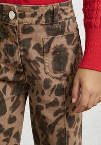Hnedé cargo nohavice s leopardím vzorom a čiernymi škvrnami, s prednou vreckom, kovovým zapínaním a priliehavým strihom.