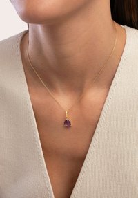 Collana in oro con ciondolo a forma di pera in gemma viola, caratterizzata da una superficie liscia e un design minimalista.