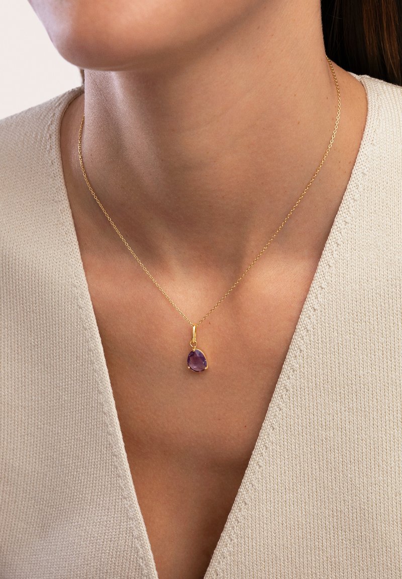 Collana in oro con ciondolo a forma di pera in gemma viola, caratterizzata da una superficie liscia e un design minimalista.