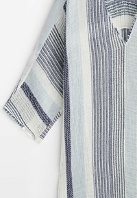 Chemise légère à manches courtes avec des rayures tissées verticales bleues et blanches et un tissu texturé, présentée sur un fond blanc uni.