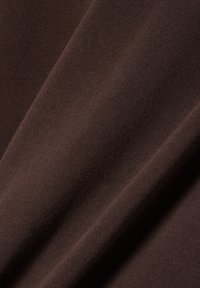 Close-up van glad, donkerbruin gebreid stuk stof met zichtbare fijne textuur en zachte plooien.