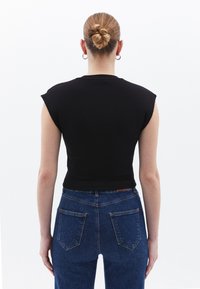 Top corto a coste nero con maniche a cappotto abbinato a jeans in denim blu a vita alta, dotato di due tasche posteriori e dettagli di cucitura visibili.