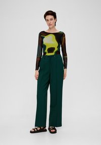 Long-sleeve, semi-sheer top with abstract pattern in green, black, and brown, paired with high-waisted, wide-leg green trousers. Black sandals.