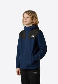 Granatowa wodoodporna kurtka z czarnymi panelami na ramionach, regulowanym kapturem i elastycznymi mankietami. Na lewej piersi znajduje się logo oraz kieszenie po bokach.