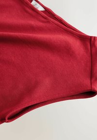 Sarkana kokvilnas auduma ar gludu tekstūru, kam piemīt liekta kakla un apakšmala. Nav redzamu rakstu vai detaļu.