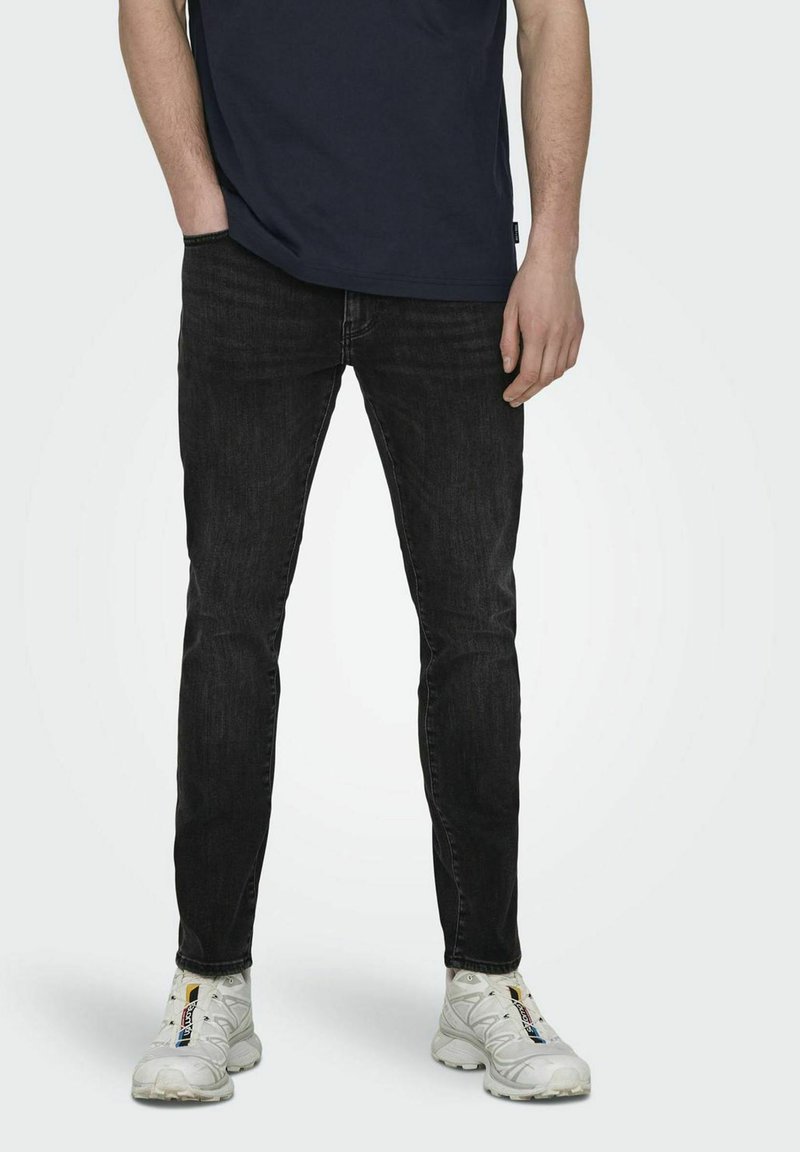 Slank passform svarte denimjeans med en falmet tekstur. Brukt med en marineblå t-skjorte og hvite joggesko. Minimalistisk design, ingen synlige logoer.