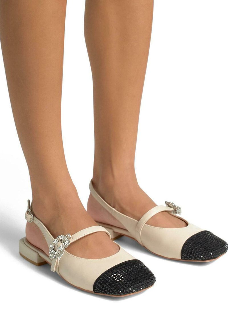 Ballerine in pelle beige con puntale nero testurizzato, caratterizzate da un accento decorativo di strass e una fascia sulla caviglia.