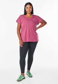 Pink short-sleeve V-neck t-shirt, black leggings, green athletic shoes with white accents, standing on a white background.