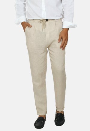 Pantaloni in lino beige con vita regolabile tramite lacci, design affusolato e orli arrotolati. Presentano una finitura testurizzata e dettagli con tasche laterali.