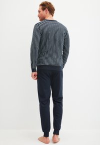 Marineblaue Schlafanzugset, bestehend aus einem gestreiften Pullover mit langen Ärmeln und passenden einfarbigen Hosen. Aus Baumwollmaterial mit elastischen Bündchen.